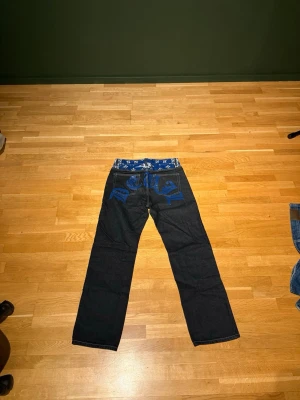 Svarta jeans från SANTO - Dom är i bra skick, köpte för många år sedan. Cool design på basksidan som sträcker sig över båda backfickorna. På byxorna står det att det är storlek M och skulle tippa att det är 32 i midja och 30 i längd 