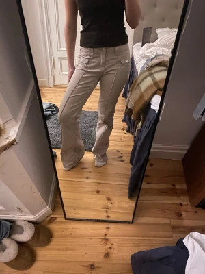 Beige bootcut-byxor från H&M Divided - Snygga beige bootcut-byxor från H&M Divided med fickor fram och bak, samt dekorativa knappar på fickorna. 