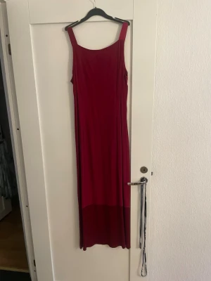 Vinröd långklänning med breda axelband - Säljer en vinröd långklänning från Forever 21 med breda axelband och rak passform. Klänningen är ärmlös och har en enkel, stilren design i mjukt material. Perfekt för dig som gillar minimalistisk stil och vill ha något bekvämt men snyggt.