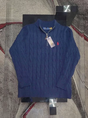 Marinblå stickad tröja Polo Ralph Lauren - Säljer en marinblå stickad tröja från Polo Ralph Lauren med kabelstickat mönster och röd logobrodering på bröstet. Tröjan har lång ärm, ribbade muddar och en half zip-dragkedja vid halsen. Perfekt för dig som gillar klassisk och stilren design.