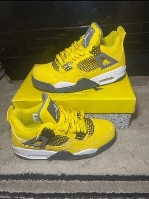 Air Jordan 4 Retro Yellow Lightning - Air Jordan 4 Retro Yellow Lightning sneakers i en fet gul färg med grå och vita detaljer. Skorna har meshpaneler, snörning och Jumpman-logga på tungan och hälen. Snygg platt sula och ikoniska detaljer som gör dem till ett måste för sneakerheads.