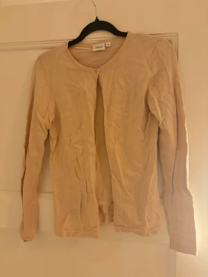 Beige kofta från Saint Tropez XS - Säljer en tunn och mjuk beige kofta från Saint Tropez i storlek XS. Koftan har rund halsringning, långa ärmar och knäppning framtill med små diskreta knappar. Perfekt att slänga över en topp när det är lite kyligt ute.