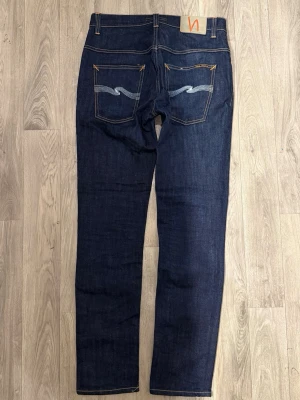 Nudie Jeans Thin Finn Dry Blå W31 L32 - Nudie Jeans Thin Finn ’Dry Ecru Embo’ i dry marinblå färg i mycket fint skick i storlek W31/L32. Dessa jeans får sin egna unika fade över tid om man använder de ofta! Mått - Midja: 39cm, Benlängd: 104,5cm. Modellen är 185cm & 63kg. Hör av dig vid funderingar!🤩