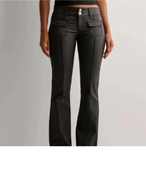 Svarta skinnbyxor nelly - Snygga svarta bootcut byxor med två framfickor med lock och dubbla knappar i midjan. Har aldrig använt! Kom gärna med prisförslag! ❤️Storlek 38 passar även olika