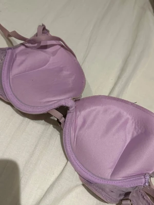 Ljuslila spets-bh med ringdetalj - Söt bh i ljuslila med vadderade kupor och spetsdetaljer över hela framsidan. Dekorativ ring i metall mellan kuporna och justerbara axelband. Insidan är slät och mjuk för extra komfort.