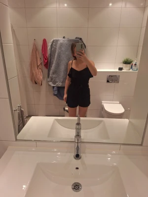 Svart byxdress från Sisters Point - Säljer en svart byxdress från Sisters Point i storlek S. Den har smala axelband, volang upptill och ett knytband i midjan för extra snygg passform. Materialet känns mjukt och lätt, perfekt för dig som vill ha en stilren look med lite edge.