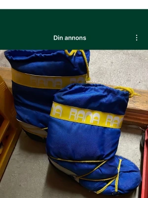 Blå Rana vinterstövlar med gul snörning - Säljer ett par blå vinterstövlar från Rana med gul snörning och gulvit logotyp runt skaftet. Stövlarna har en rejäl platt sula med grovt mönster för extra grepp. Yttermaterialet är syntet och de är fodrade för att hålla värmen under kalla dagar. Säljs på fler sidor.