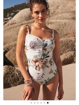 Vit blommig baddräkt med axelband - Supersnygg baddräkt i vitt med stora blommor i pastelliga färger. Axelbanden är smala och svtagbara, modellen har rynkade detaljer och en slimming effect. Perfekt för stranden eller poolen och ger en fräsch sommarkänsla. 