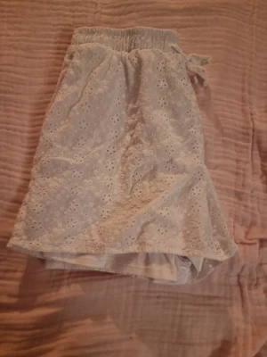 Vita broderade shorts med snörning - Säljer ett par ljusa, vita shorts med elastisk midja och snörning framtill. Shortsen har ett blommigt broderat mönster och är fodrade med ett mjukt innerfoder. Perfekta för varma sommardagar och ger en söt och avslappnad vibe.