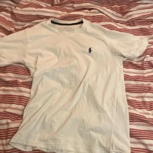 Vit USPA t-shirt i bomull - Vit klassisk t-shirt från USPA i storlek S. T-shirten har korta ärmar och en liten blå logga broderad på bröstet. Tillverkad i mjuk bomull och har en rund halsringning med svart kant på insidan. Perfekt för chill dagar och enkel att matcha.
