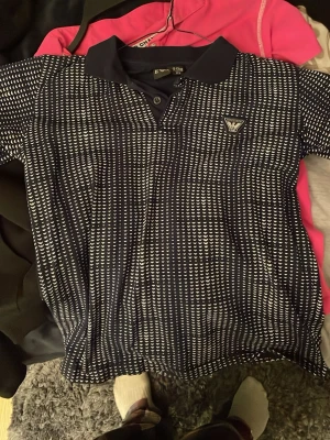 Mörkblå EVA skjorta med mönster - Snygg mörkblå skjorta från EVA i storlek 152, passar dig som är 12-13 år. Skjortan har ett vitt, prickigt mönster över hela tyget och klassisk krage med knappar framtill. Perfekt för dig som gillar stilrena detaljer och vill sticka ut lite extra.