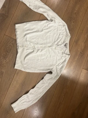 Vit kofta  - Säljer en klassisk vit kofta från H&M i storlek S. Koftan har långa ärmar, rund hals och knäppning med vita knappar framtill. Materialet är mjukt och stickat, perfekt för lager-på-lager under kyliga dagar. Enkel och stilren design som funkar till många outfits.