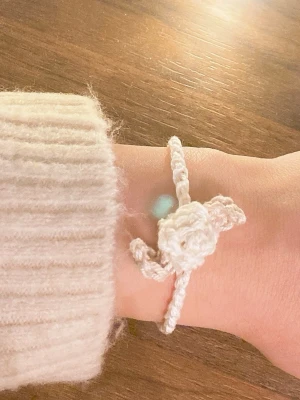 Handvirkad vit blomarmband - Unikt handvirkat armband i vit färg med en söt blomma i mitten och blad på sidorna. Armbandet är gjort av mjukt garn och har en enkel, bohemisk stil som passar perfekt för dig som gillar personliga accessoarer.