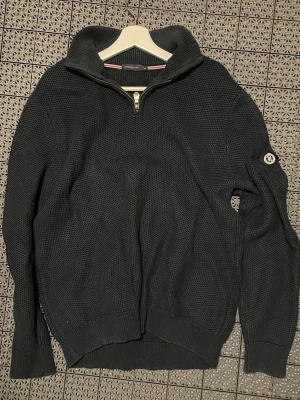 Mörkblå stickad tröja Henri Lloyd - Säljer en mörkblå stickad tröja från Henri Lloyd i storlek L. Tröjan har en grovstickad struktur, hög krage och en snygg half zip-dragkedja framtill. Långa ärmar och diskret logga på ena ärmen. Perfekt för kyliga dagar.