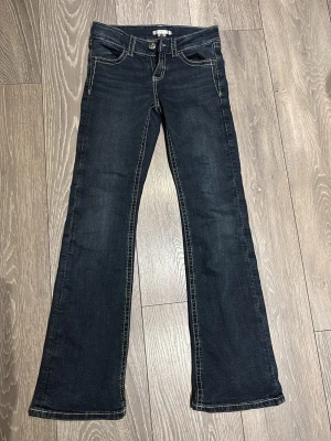 Mörkblå bootcut jeans med broderade fickor - Snygga mörkblå jeans med bootcut-snitt och kontrastsömmar. Baksidan har två fickor med detaljerade broderier i beige. Jeansen har klassisk femficksdesign och är tillverkade i jeansmaterial med en skön passform.