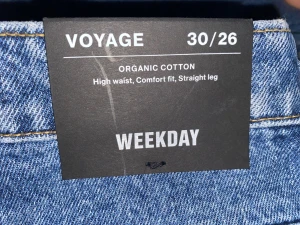 Weekday Voyage blå jeans 30/26 - Snygga blå jeans från Weekday, modell Voyage. De är tillverkade i 100% ekologisk bomull och har hög midja, raka ben och en komfortabel passform. Klassisk femficksdesign med tydliga kontrastsömmar och knappstängning framtill. Har aldrig använd de dem inte passar prislapp och allt är kvar