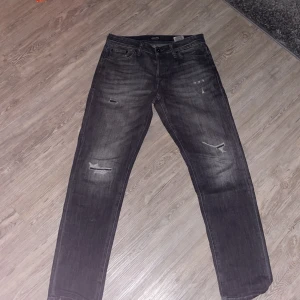 Svarta tapered jeans från Jack & Jones - Säljer ett par svarta jeans från Jack & Jones, modell Tapered/Mike. Jeansen har slitna detaljer och snygga rippade partier på framsidan. Klassisk femficksdesign och rak passform med avsmalnande ben. Perfekt för dig som gillar en avslappnad streetstil. Pris går att diskutera, skriv för minsta fundering✅
