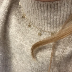 Guldigt halsband med stjärnhängen - Snyggt halsband i guldton med små stjärnor som hänger längs en tunn kedja. Perfekt för dig som gillar detaljer och vill ha något som sticker ut lite extra. Kedjan är smal och stjärnorna har en blank finish som fångar ljuset fint. Lite rostig på några stjärnor men syns knappt.