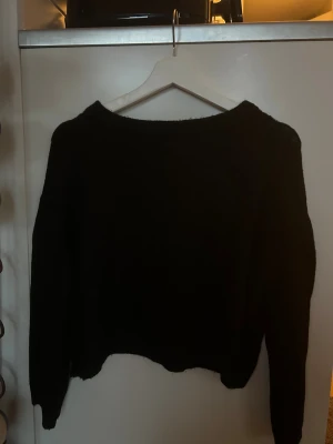 Svart stickad tröja med loose fit - Svart stickad tröja med avslappnad loose passform och långärmade ärmar. Tröjan har en enkel design med rund hals och mjukt material som gör den skön att bära. Perfekt för dig som gillar en stilren och chill look. (lite kortare)