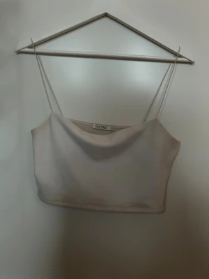 Vit croppad linnetopp från NLY One - Säljer en stilren vit croppad linnetopp från NLY One med tunna axelband. Toppen har en enkel och clean design som är lätt att matcha med olika outfits. Perfekt för varma dagar och chill häng med vänner. (ljsuet gör att den ser missfärgad ut)