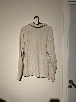 Beige pikétröja från Weekday - Säljer en stilren beige pikétröja från Weekday med klassisk krage och v-ringad hals. Tröjan har lång ärm och är gjord i mjuk bomull som känns skön mot huden. Perfekt för dig som gillar enkel och clean stil.