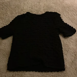 Svart topp från Lindex - Säljer en svart topp från Lindex i storlek M. Toppen har ett ribbat och texturerat tyg med korta ärmar och rund hals. Materialet känns mjukt och stretchigt, perfekt för dig som gillar en enkel men cool look. Kan stylas med jeans eller kjol för en chill vibe. Knappt använd och inget tecken på användning. Skriv för mer bilder + frågor! 