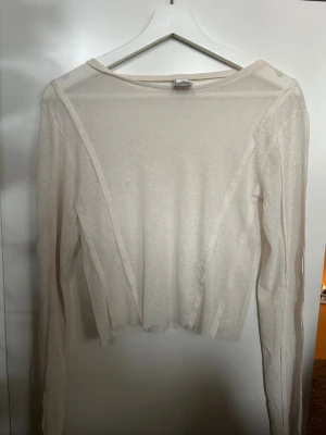 Beige långärmad mesh-top - Säljer en tunn och transparent beige långärmad topp i mesh. Toppen har en enkel och clean design med rund hals och synliga sömmar som ger en cool detalj. Perfekt att styla lager på lager eller med ett linne under för en trendig look.