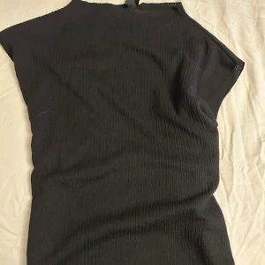 Svart ribbad topp - Snygg svart topp med ribbad struktur och ärmlös design. Toppen har en enkel, rak passform som sitter tight och är perfekt för dig som gillar minimalistisk stil. Materialet känns mjukt och följsamt mot kroppen.