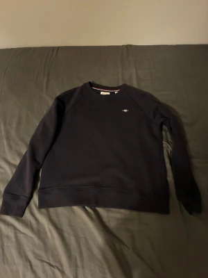 Mörkblå sweatshirt från GANT - Snygg mörkblå sweatshirt från GANT med rund hals och broderad logga på bröstet. Tröjan har långa ärmar och ribbade muddar vid ärmslut och nederkant. Perfekt för dig som gillar klassisk och enkel stil.