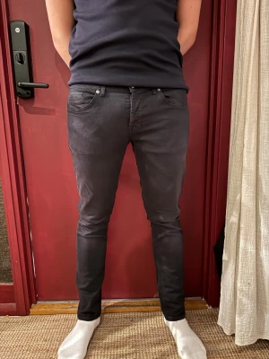 Svarta skinny jeans från Dondup - Svarta jeans från Dondup med slim passform och klassisk femficksdesign. Snygga detaljer som metallknappar och Dondup-logga på bakfickan. Nypris 2400. Storlek 35. Modellen på bilden är 189cm och 87kg. Använda ett fåtal gånger. 