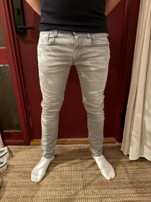 Replay ljusgrå slim jeans - Snygga ljusgrå jeans från Replay med slim passform och klassisk femficksdesign. Byxorna har svarta Replay-detaljer vid linningen och bakfickorna har diskret broderi. Storlek 32. Modellen på bilden är 189cm och 87kg. Nypris 1200. 