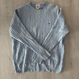 Ljusblå stickad tröja Park Lane XL - Snygg ljusblå stickad tröja från Park Lane i storlek XL. Tröjan har ett klassiskt kabelstickat mönster, rund hals och ribbade muddar. Diskret broderad logga på bröstet ger en clean look. Perfekt för dig som gillar stilrena och bekväma plagg.