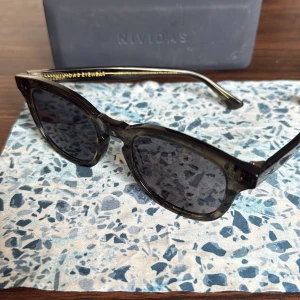 Svarta solglasögon Nividas Sydney - Snygga solglasögon från Nividas, modell Sydney. Runda bågar i mörkgrönt och svart glas med lätt transparent finish. Kommer med originalfodral. Nypris 1200kr