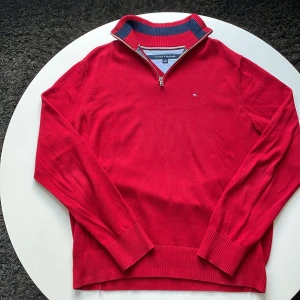 Röd half zip tröja Tommy Hilfiger - Snygg röd tröja från Tommy Hilfiger med half zip och ribbad krage i rött och marinblått. Liten logga på bröstet och långa ärmar. Tröjan är gjord i mjuk bomull och har breda muddar vid ärmslut och nederkant. Perfekt för dig som gillar klassisk stil.