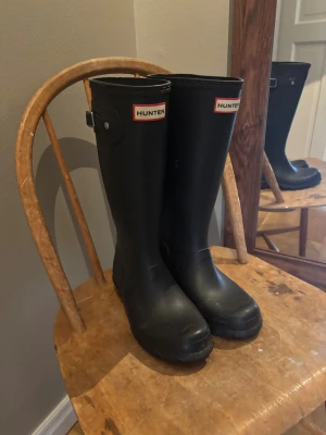 Hunter stövlar - Klassiska svarta Hunter stövlar i gummi med rund tå och platt sula. Höga skaft och tydlig Hunter-logga framtill. Perfekta för regniga dagar och leriga äventyr. Kan vara i barnmodell är lite osäker men tror inte det spelar någon roll🩷