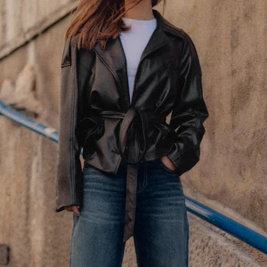 Svart skinnjacka med bälte från Zara - Snygg svart skinnjacka från Zara med knappar framtill och ett bälte i midjan. Perfekt nu till hösten/våren. Säljer helt ny med prislappen på då jag köpte fel storlek men glömde att lämna tillbaka. Jackan är i en storlek L, men sitter mer som en M, snygg oversized!