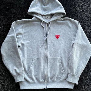 CDG Hoodie  - Grå hoodie från Comme des Garçons Play med dragkedja, snörning och huva. Framtill finns ett rött hjärta med ögon broderat, och på ryggen flera röda hjärtan samt PLAY-loggan. Skick 7/10 i använt skick, storlek L, pris går att diskutera✅