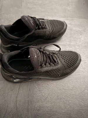 Nike Air Max 270 svarta sneakers - Svarta Nike Air Max 270 sneakers med ventilerande mesh-ovandel och synlig Air-enhet i hälen. Snygg sportig design med snörning och rund tå. Perfekt för dig som gillar streetstyle och vill ha bekväma skor med grym dämpning.