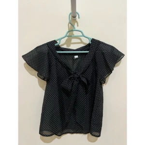 Svart prickig blus med knyt - Säljer en svart blus från Divided med vita prickar och v-ringning. Blusen har korta, luftiga ärmar och ett snyggt knyt framtill. Supersöt och trendig topp för dig som gillar prickigt!