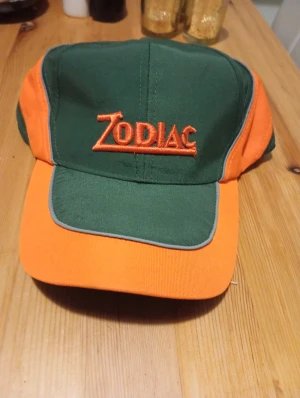 Grön och orange Zodiac keps - Snygg keps från Zodiac i grön och orange med broderad logga framtill. Kepsen har klassisk form med böjd skärm och kontrastfärgade paneler. Perfekt för dig som vill sticka ut med färg och stil.