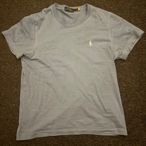 Ljusblå t-shirt från Polo Ralph Lauren - Ljusblå t-shirt från Polo Ralph Lauren med klassisk rund hals och korta ärmar. Ikonisk broderad logga i vitt på bröstet. Tillverkad i mjuk bomull som känns skön mot huden. Perfekt för en clean och stilren look. Storlek S, 100% bomull