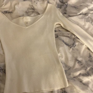 Vit ribbad långärmad topp H&M - Säljer en helt ny och oanvänd vit ribbad långärmad topp från H&M i storlek XS. Toppen har v-ringad hals och är figurnära med stretchigt material. Perfekt att styla med jeans eller kjol för en clean och fräsch look. Superenkel att matcha med andra plagg!