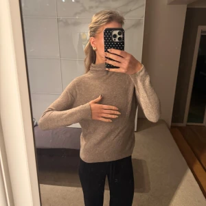 Beige polotröja i mjuk ull - Säljer en beige polotröja med lång ärm och hög krage. Tröjan är i mjuk och skön ull, perfekt för kyliga dagar. Enkel och stilren design som är lätt att matcha med olika outfits. Passformen är normal och materialet känns lyxigt mot huden.