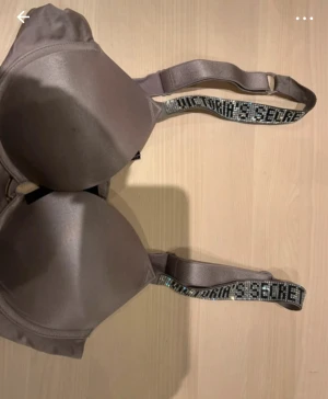 Champagnefärgad korsett från Victoria's Secret - Champagnefärgad korsett från Victoria's Secret med glittriga axelband där märket står i stora bokstäver. Snygg och stilren design med slät yta och lätt vadderade kupor. Perfekt för dig som vill ha något extra till outfiten.