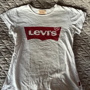 Vit Levi's t-shirt med rött tryck - Vit t-shirt från Levi's med det klassiska röda logotrycket på bröstet. T-shirten har korta ärmar, rund halsringning och är gjord i mjuk bomull. Perfekt för en avslappnad och cool stil.