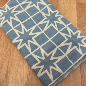 Blåvit halsduk från By Malina - Snygg halsduk från By Malina i blått och vitt med grafiskt stjärnmönster. Tillverkad i en mjuk ullblandning som känns skön mot huden. Perfekt accessoar för att lyfta din outfit med lite extra färg och mönster.