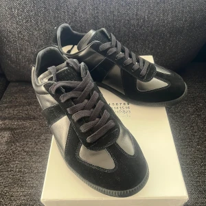 Maison Margiela svarta sneakers i skinn - Tjena! Lyxiga Maison Margiela sneakers i svart skinn och mocka med klassisk rund tå och platt sula då. Snygga svarta snören. Perfekt för dig som gillar minimalistisk och stilren design! Box tillkommer