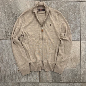 Morris Full zip - Snygg beige kofta från Morris i 100% merinoull med dragkedja framtill och diskret broderad logga på bröstet. Tröjan är använd endast ett fåtal gånger så den är i väldigt bra skick. Nypris: 1999kr. Hör av dig vid funderingar!