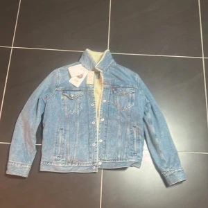 Levi's blå teddyjeansjacka Jacquard L - Helt ny Blå jeansjacka från Levi's med mjukt teddyfoder i beige. Klassisk modell med knappar framtill, två bröstfickor med lock och lång ärm. Jacquard by Google-tag på insidan. Perfekt för dig som vill ha tech och stil i ett. Ny pris 1400