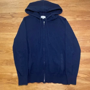 Mörkblå stickad hoodie - Mörkblå hoodie med dragkedja från Braidbelt UF i storlek S. Tröjan har huva med snörning, ribbade muddar och är tillverkad i ett stickat material som känns mjukt och skönt. Perfekt för dig som gillar enkel och stilren design.